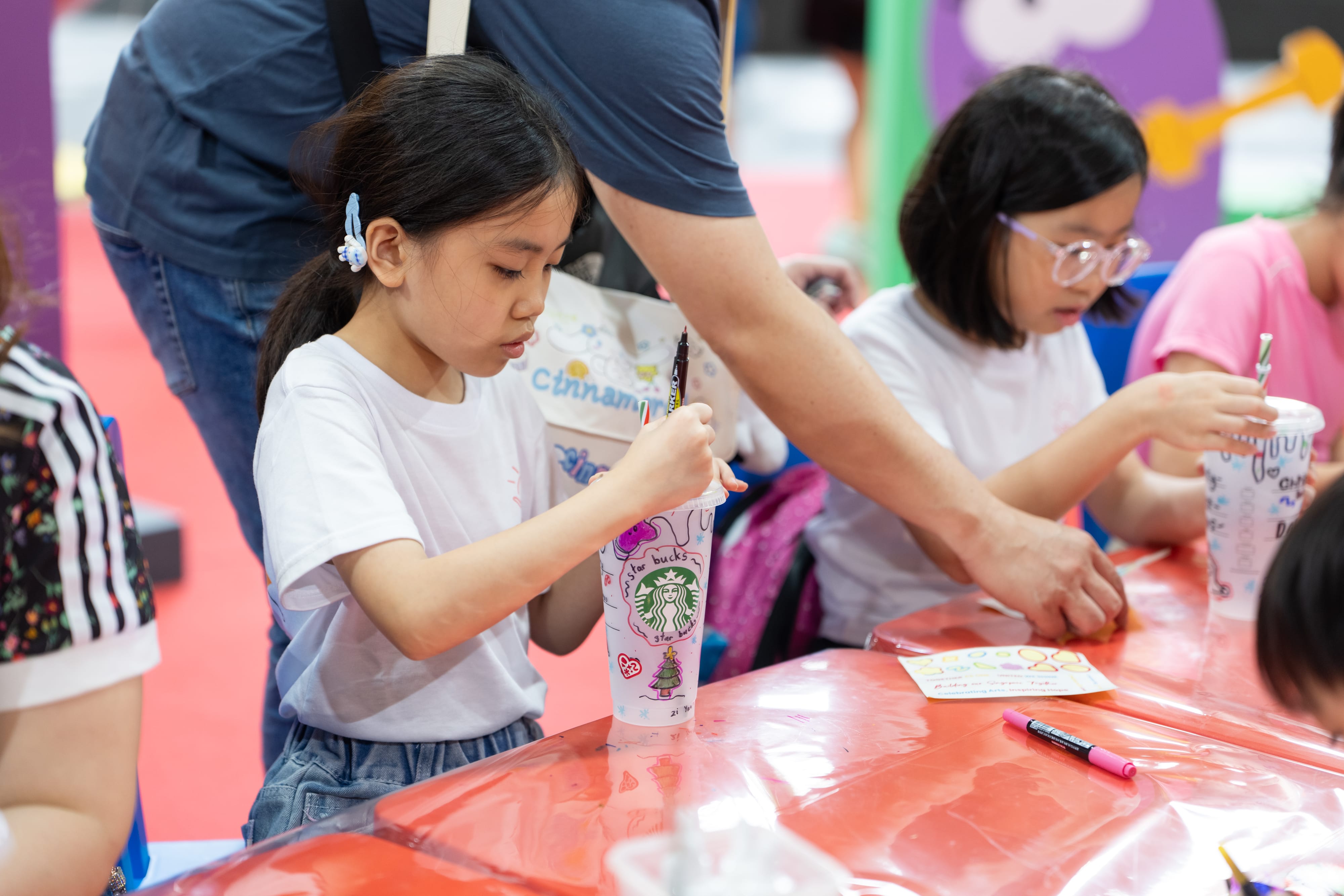 Girl decorating a translucent Starbucks cup with coloured markers.